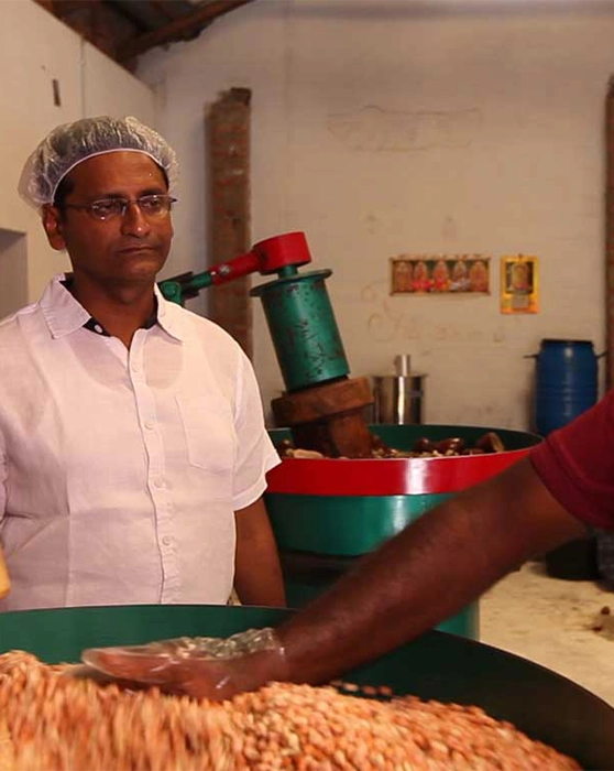 A person in a white shirt standing near a machine processing food with peanuts in the foreground.